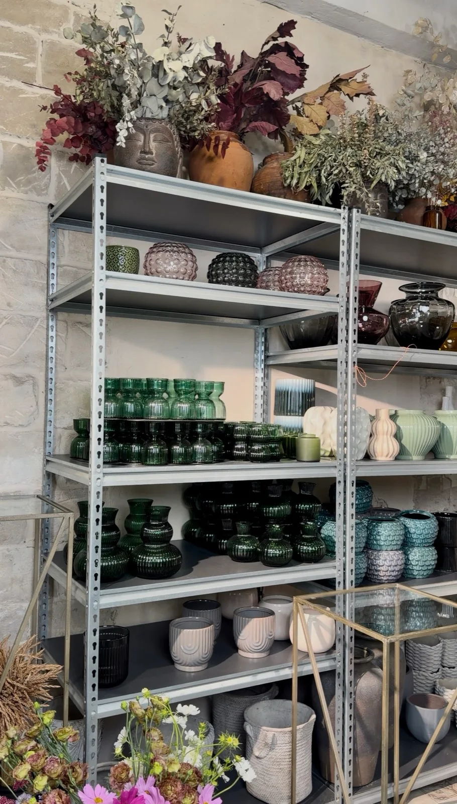 Un modul de rafturi BOX plin cu vaze din sticlă verde și chihlimbarie și ghivece din ceramică